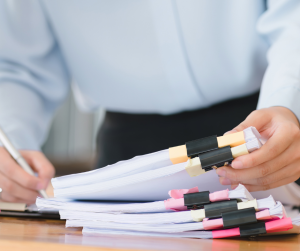 Person organizing stacked paper documents on desk