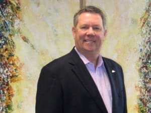 Man smiling in suit before abstract painting.