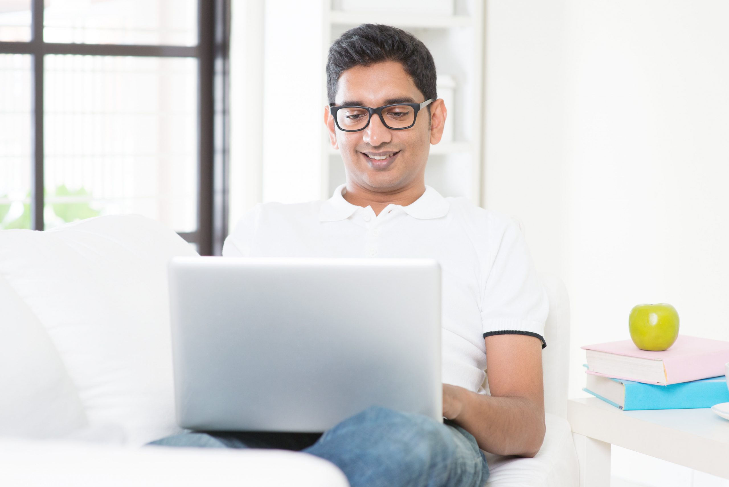 Man smiling using laptop on white couch.