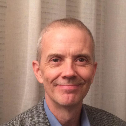 Smiling man with grey hair in front of curtain.