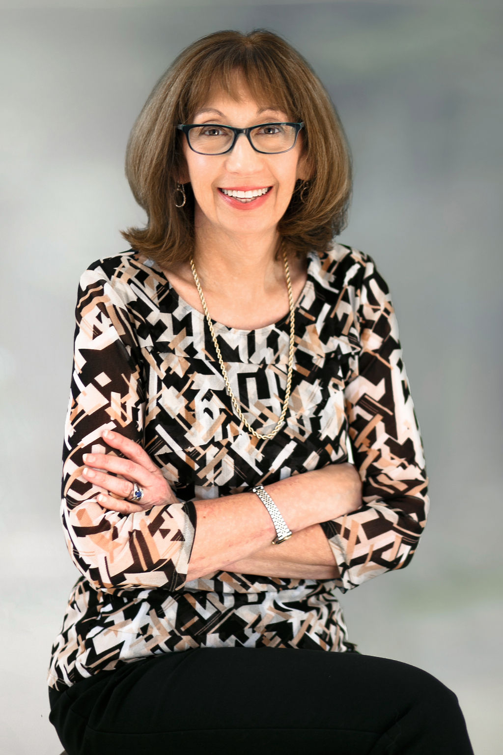 Professional smiling woman in patterned blouse and glasses.