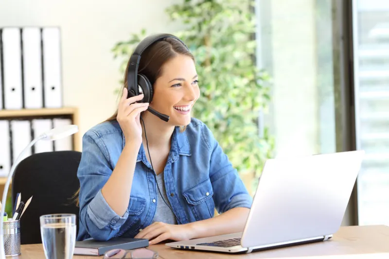 Smiling woman with headset at laptop, working from home.