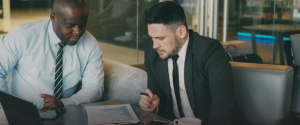 Two businessmen discussing outsourced accounting documents at a desk.