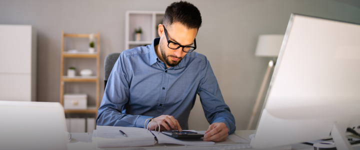 outsourced accountant using calculator at desk with computer.